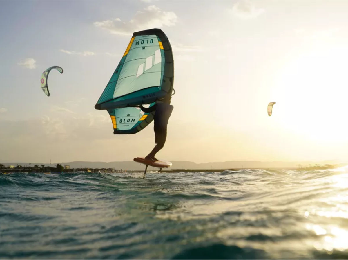group of people on the beach watching a kitesurfer jump. everyone is wearing a kite tribe tshirt