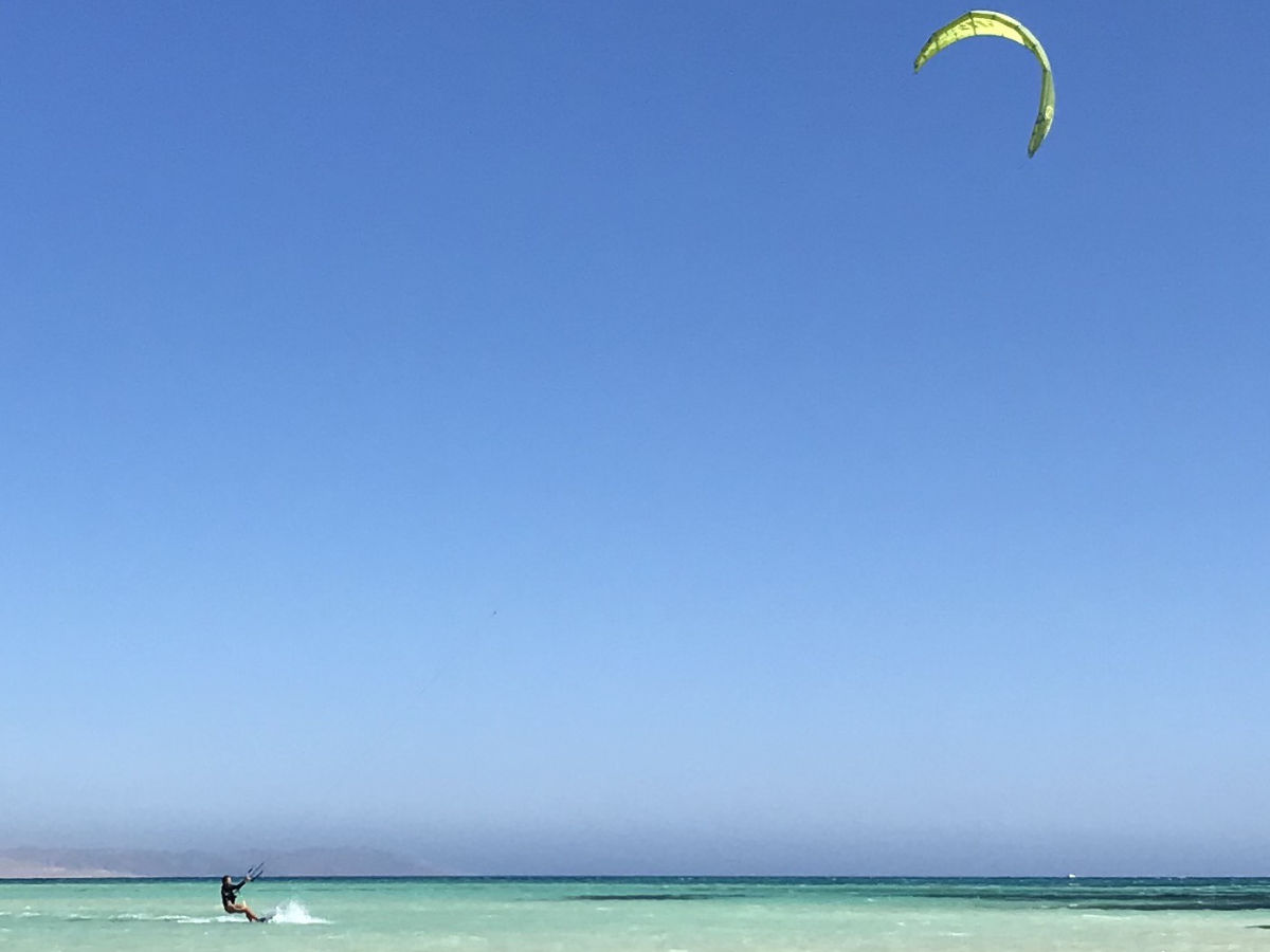 group of 5 girls sitting on the kite beach in El Gouna in Egypt, looking at the kites in the water. The image shows the girls from the back, all wearing a Kite Tribe T-Shirt