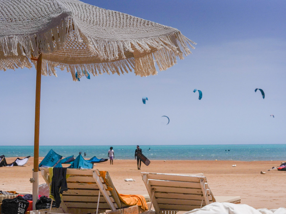 group of 5 girls sitting on the kite beach in El Gouna in Egypt, looking at the kites in the water. The image shows the girls from the back, all wearing a Kite Tribe T-Shirt