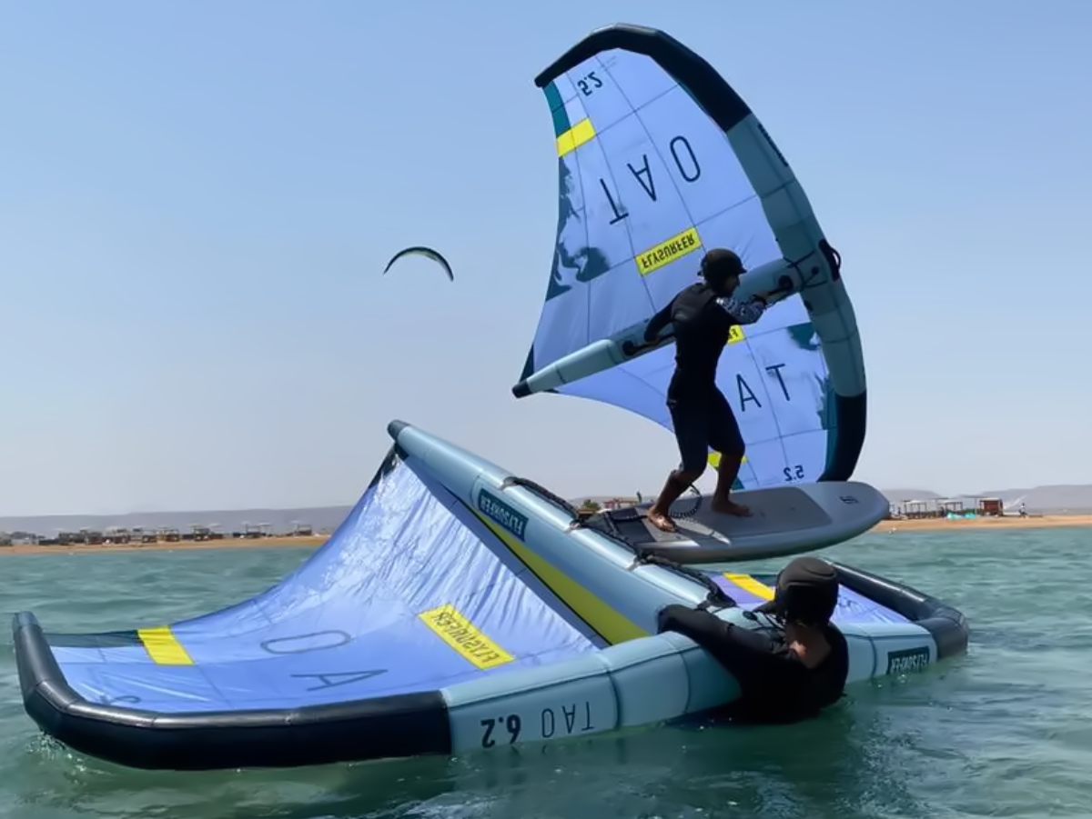 group of 5 girls sitting on the kite beach in El Gouna in Egypt, looking at the kites in the water. The image shows the girls from the back, all wearing a Kite Tribe T-Shirt