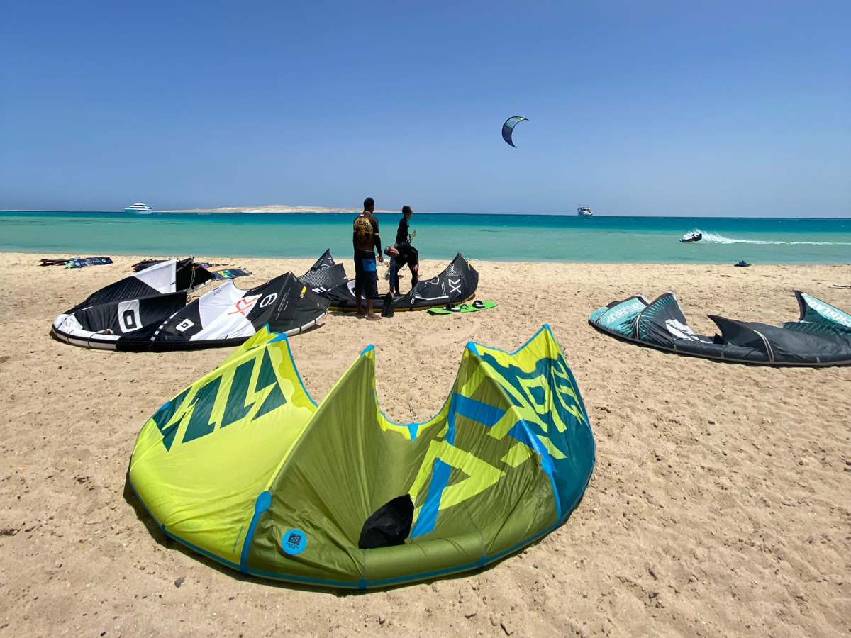 group of 5 girls sitting on the kite beach in El Gouna in Egypt, looking at the kites in the water. The image shows the girls from the back, all wearing a Kite Tribe T-Shirt