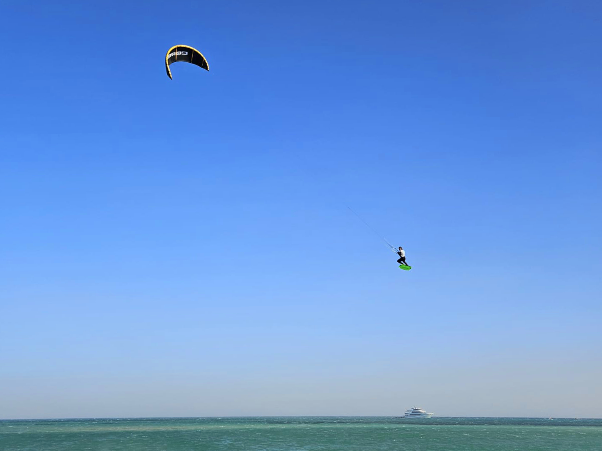 group of 5 girls sitting on the kite beach in El Gouna in Egypt, looking at the kites in the water. The image shows the girls from the back, all wearing a Kite Tribe T-Shirt
